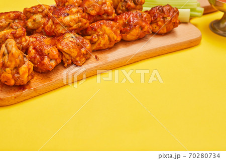 Buffalo chicken wings on a wooden board with celery on a yellow background, copy space 70280734