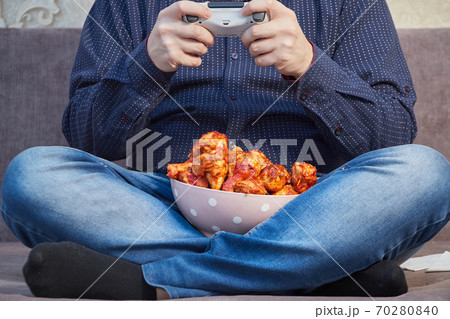 man playing on the couch with a plate of Buffalo Chicken Wings, copy space 70280840