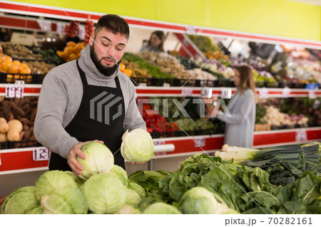Male shop assistant lays fresh cabbage on counter in grocery shop Male shop assistant lays fresh cabbage on counter in grocery shop 70282161