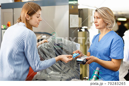 Female customer paying with bank card for service at dry-cleaning salon 70283265
