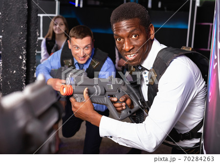 Men and women in business suits playing laser tag emotionally in dark room Men and women in business suits playing laser tag emotionally in dark room 70284263