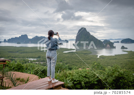 View of a traveler using her mobile phone taking a photo of Sametnangshe island in Phang-nga. View of a traveler using her mobile phone taking a photo of Sametnangshe island in Phang-nga. 70285574