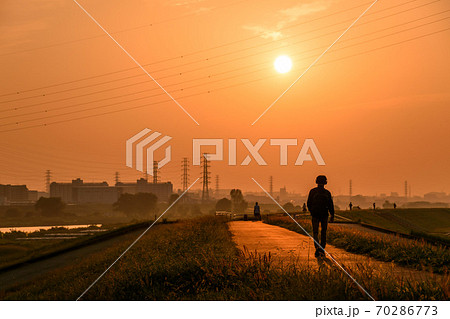 埼玉県 土手を歩く人と夕日の写真素材