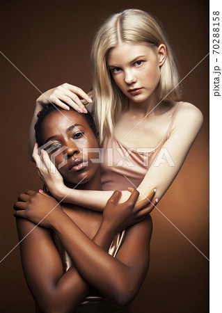 two pretty girls african and caucasian blond posing cheerful together on brown background, diverse lifestyle people concept 70288158