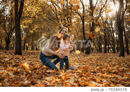 Happy family mom and toddler baby girl playing outdoors in fall park. Little girl and her mother in the autumn park Happy family mom and toddler baby girl playing outdoors in fall park. Little girl and her mother in the autumn park 70289379