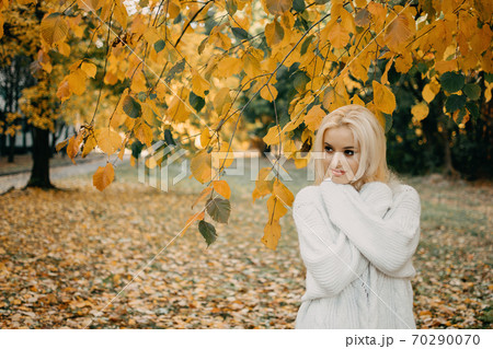 Beautiful blonde Woman with Autumn Leaves on Fall Nature Background. Alone brooding woman in white sweater enjoys fall nature Beautiful blonde Woman with Autumn Leaves on Fall Nature Background. Alone brooding woman in white sweater enjoys fall nature 70290070