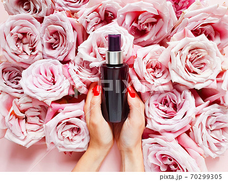Mockup of dark brown spray bottle, caucasian female hands with red nails and roses on pink table. Top view, copy space Mockup of dark brown spray bottle, caucasian female hands with red nails and roses on pink table. Top view, copy space 70299305