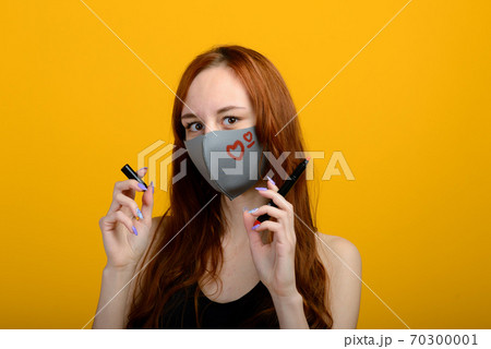 Portrait of a girl in a medical mask, which puts on a rubber gloves. Yellow and grey background. 70300001