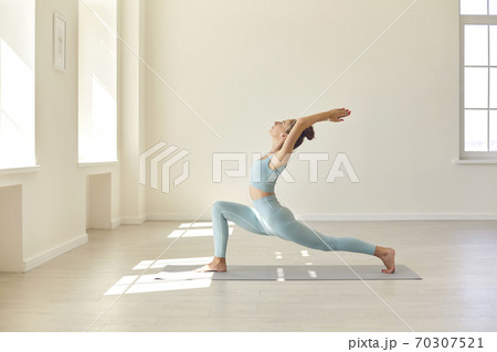 Beautiful young woman in activewear doing Crescent Lunge asana while practicing yoga in gym Beautiful young woman in activewear doing Crescent Lunge asana while practicing yoga in gym 70307521