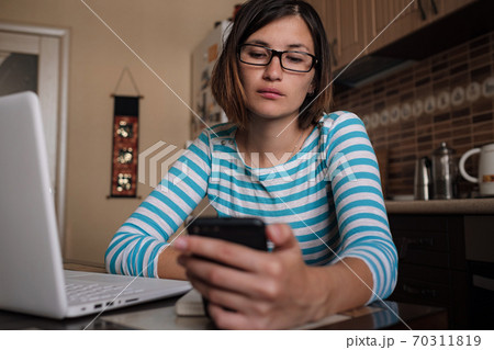Young woman sitting in kitchen and working on laptop in morning. Female using laptop dining table 70311819