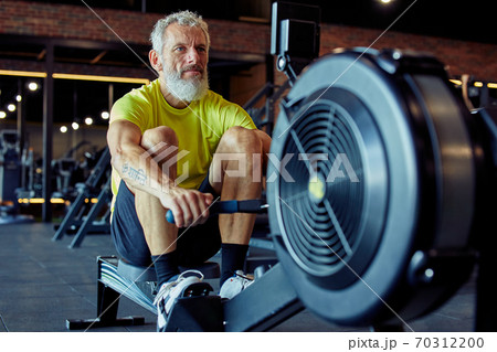 Sport and fitness after 50. Strong mature athletic man in sportswear exercising on rowing machine at gym 70312200