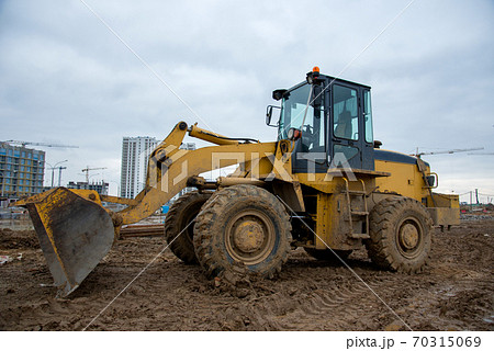 Front-end loader working at construction site. Earth-moving heavy equipment for road work. Front-end loader working at construction site. Earth-moving heavy equipment for road work. 70315069