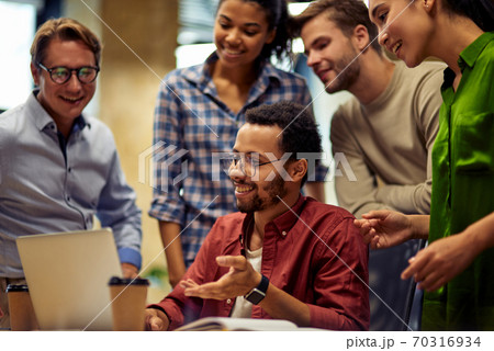 Group of happy multiracial business people looking at laptop screen and discussing work or project results while standing in the modern office or coworking space Group of happy multiracial business people looking at laptop screen and discussing work or project results while standing in the modern office or coworking space 70316934