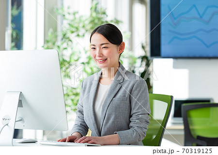 明るいオフィスの窓側でパソコン操作する若いビジネスウーマン 70319125