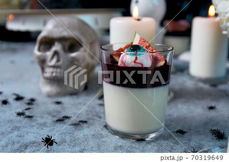 Curd dessert with raspberry jam. Garnished with fig slices and eye candy. Dessert for halloween. In the background burning candles and a skull Curd dessert with raspberry jam. Garnished with fig slices and eye candy. Dessert for halloween. In the background burning candles and a skull 70319649