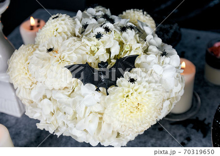 A bouquet of white chrysanthemums and hydrangeas, decorated with a black bat and confetti in the form of black spiders. Halloween holiday concept 70319650