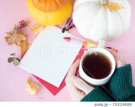Hands holding cup of tea near white paper on red envelope with autumn leaves and pumpkins around Hands holding cup of tea near white paper on red envelope with autumn leaves and pumpkins around 70324689