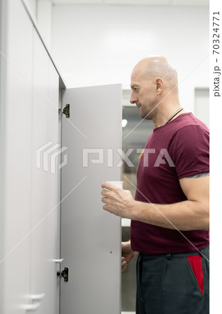 Side view of bald mature worker of factory standing in front of open locker Side view of bald mature worker of factory standing in front of open locker 70324771