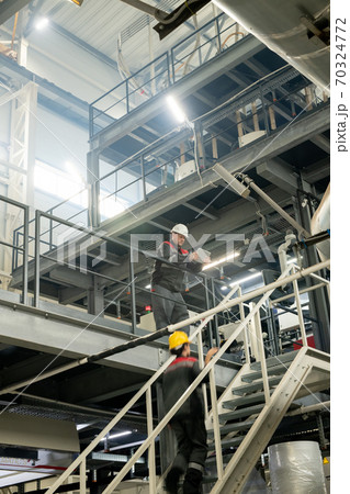 Foreman with tablet bending over staircase where female worker moving upwards Foreman with tablet bending over staircase where female worker moving upwards 70324772
