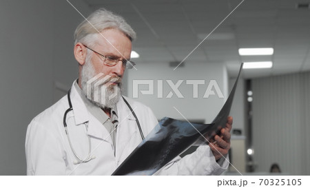 Elderly male doctor examining x-ray scans of a patient Elderly male doctor examining x-ray scans of a patient 70325105