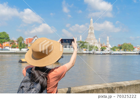 Asian woman, a tourist people, travelling, taking a photo with smartphone in Temple of Dawn or Wat Arun and Chao Phraya River, Bangkok, Thailand. Urban old town city in holiday vacation. Lifestyle Asian woman, a tourist people, travelling, taking a photo with smartphone in Temple of Dawn or Wat Arun and Chao Phraya River, Bangkok, Thailand. Urban old town city in holiday vacation. Lifestyle 70325222