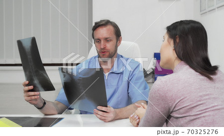Mature male surgeon examining x-ray scans of a female patient 70325276