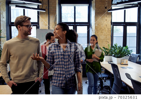 After team meeting. Two young diverse business people, male and female coworkers talking about something while walking in the modern office After team meeting. Two young diverse business people, male and female coworkers talking about something while walking in the modern office 70325631