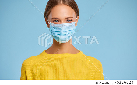 young woman in a protective medical mask and yellow sweater against a blue background in the midst of the coronavirus pandemic. young woman in a protective medical mask and yellow sweater against a blue background in the midst of the coronavirus pandemic. 70326024