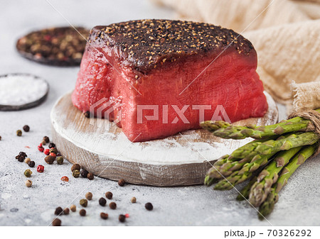 Slice of Raw Beef Topside Joint with Salt and Pepper on round chopping board with asparagus tips Slice of Raw Beef Topside Joint with Salt and Pepper on round chopping board with asparagus tips 70326292