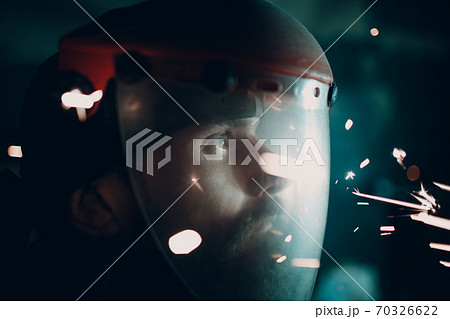 Man in transparent protective mask with flying sparks in darkness. 70326622