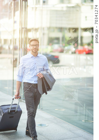 Going to airport terminal. Vertical shot of a young confident businessman walking on city streets and pulling his suitcase Going to airport terminal. Vertical shot of a young confident businessman walking on city streets and pulling his suitcase 70341274
