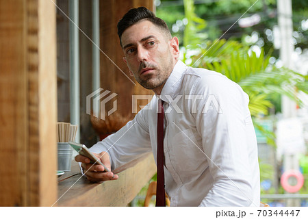 Portrait of businessman thinking while using phone at the coffee shop 70344447