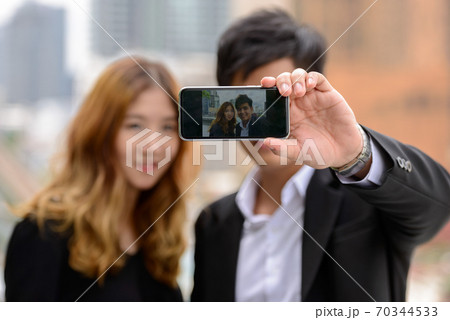Happy young Asian business couple taking selfie together in the city Happy young Asian business couple taking selfie together in the city 70344533