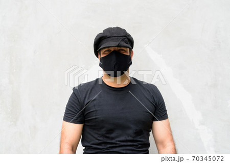Portrait of Persian man wearing hat and mask against concrete wall 70345072