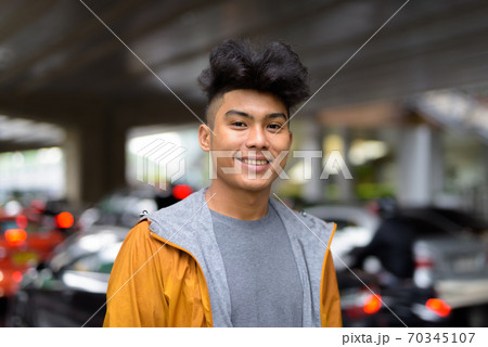 Happy young Asian man with curly hair smiling in the city streets 70345107