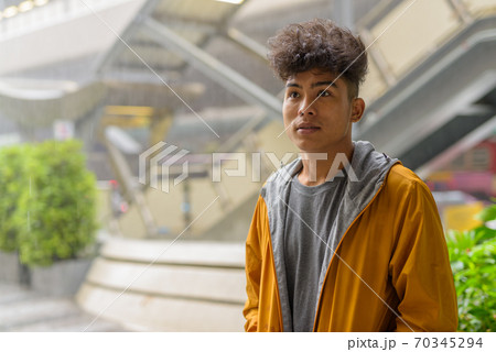 Young Asian man with curly hair sitting in the city outdoors with rain 70345294
