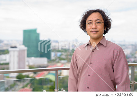 Japanese businessman with curly hair wearing eyeglasses against view of the city Japanese businessman with curly hair wearing eyeglasses against view of the city 70345330