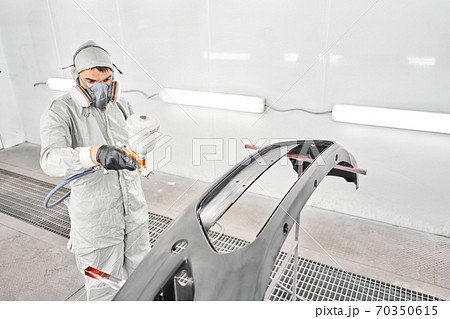 Worker painting parts of the car in special painting chamber, wearing costume and protective gear. Car service station. Worker painting parts of the car in special painting chamber, wearing costume and protective gear. Car service station. 70350615