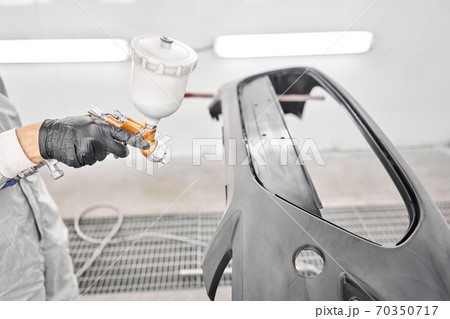 Worker painting parts of the car in special painting chamber, wearing costume and protective gear. Car service station. 70350717