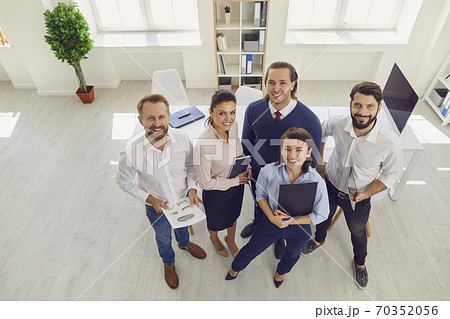 Satisfied Sales Department employees standing in company office looking at camera Satisfied Sales Department employees standing in company office looking at camera 70352056