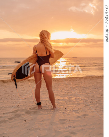 Surfer girl on sand beach with surfboard at warm sunset or sunrise. Attractive surfer women on beach Surfer girl on sand beach with surfboard at warm sunset or sunrise. Attractive surfer women on beach 70354737