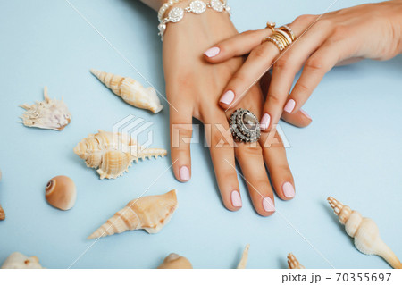 beautiful woman hands with pink manicure holding sea shells, lot of rings on fingers on blue background, luxury jewelry concept 70355697