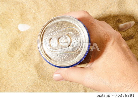 Woman hand takes cold beer or soda can with water drops from sea sand on a sunny day. Woman hand takes cold beer or soda can with water drops from sea sand on a sunny day. 70356891