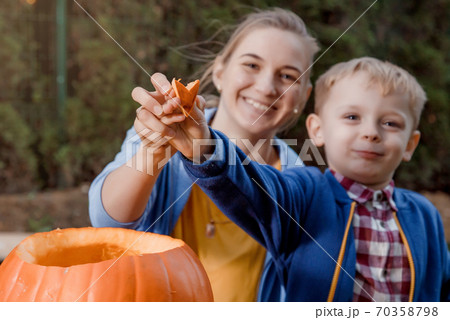 A boy and his mother cut a pumpkin. A young mother and son are preparing a pumpkin for Halloween. Preparing for Halloween. Peel an orange pumpkin. 70358798