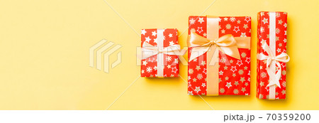 wrapped Christmas or other holiday handmade present in paper with gold ribbon on yellow background. Present box, decoration of gift on colored table, top view 70359200