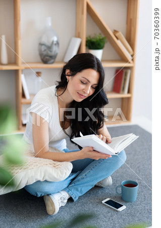 Cute young woman reading a book while sitting at home on a weekend. 70360399