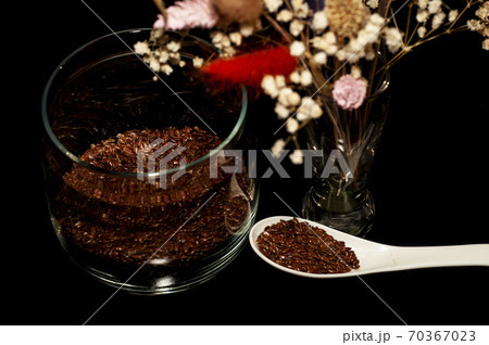 vertical art photo of flax seeds in a jar and spoon with a bouquet of dried flowers on a black background 70367023