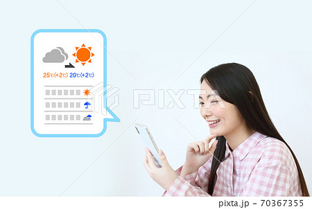 スマホで天気予報を調べるパジャマ姿の女性イメージ 70367355