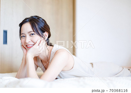 ベッドで頬杖を突いて横たわる女性の写真素材
