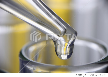Chemical pipette dispenser drips yellow liquid into glassware closeup 70373498